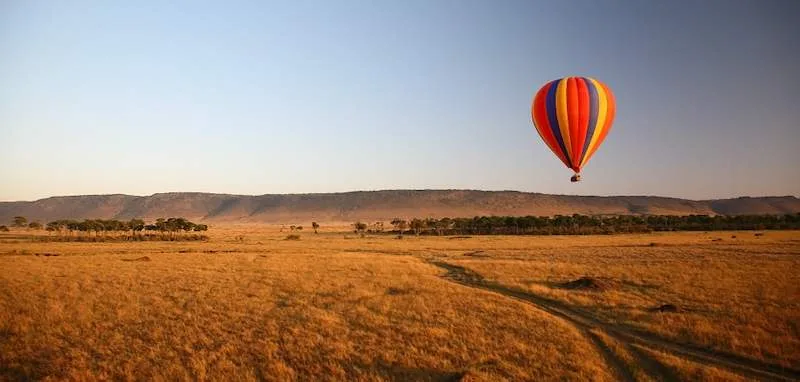 A hot-air balloon floats over the Mara grasslands at sunrise.