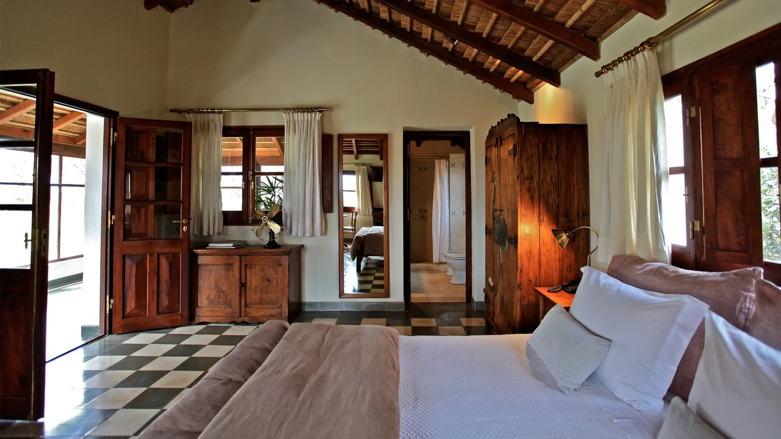 A timber-beamed guest bedroom with a four-poster bed and open doors to greenery.