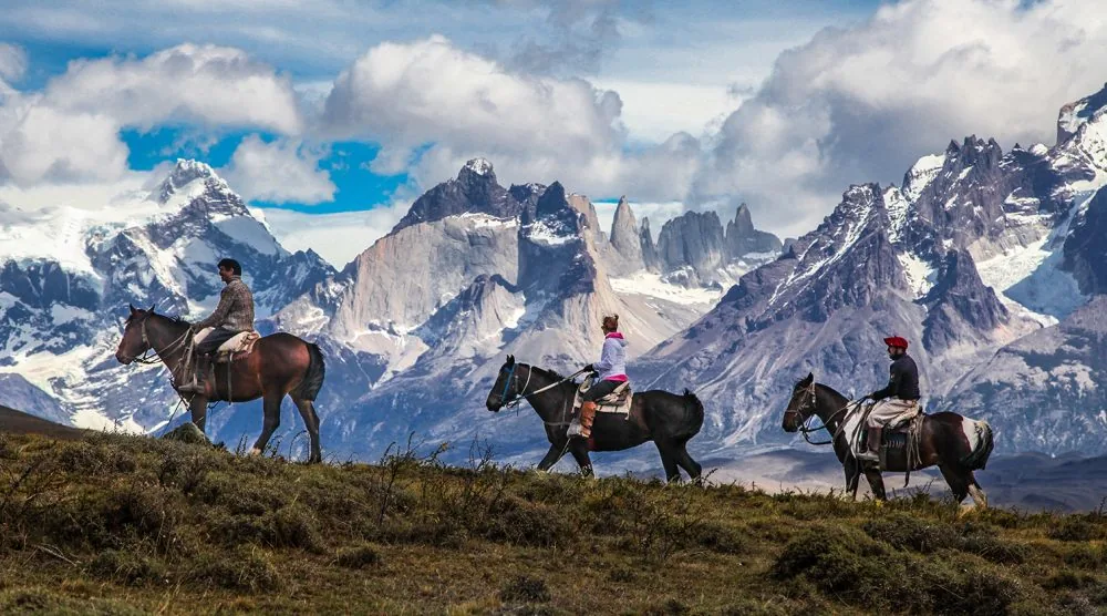 Riders cross the Patagonian foothills on horseback.