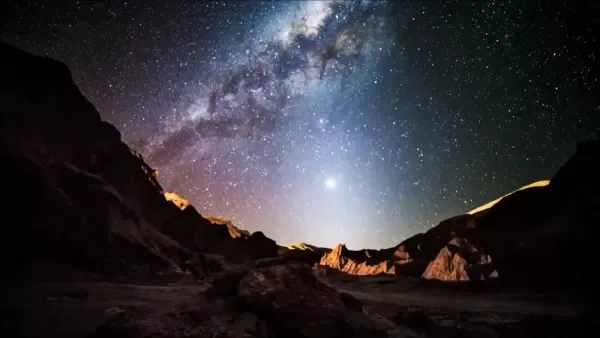 Two visitors look up at the Milky Way over a dark desert landscape.