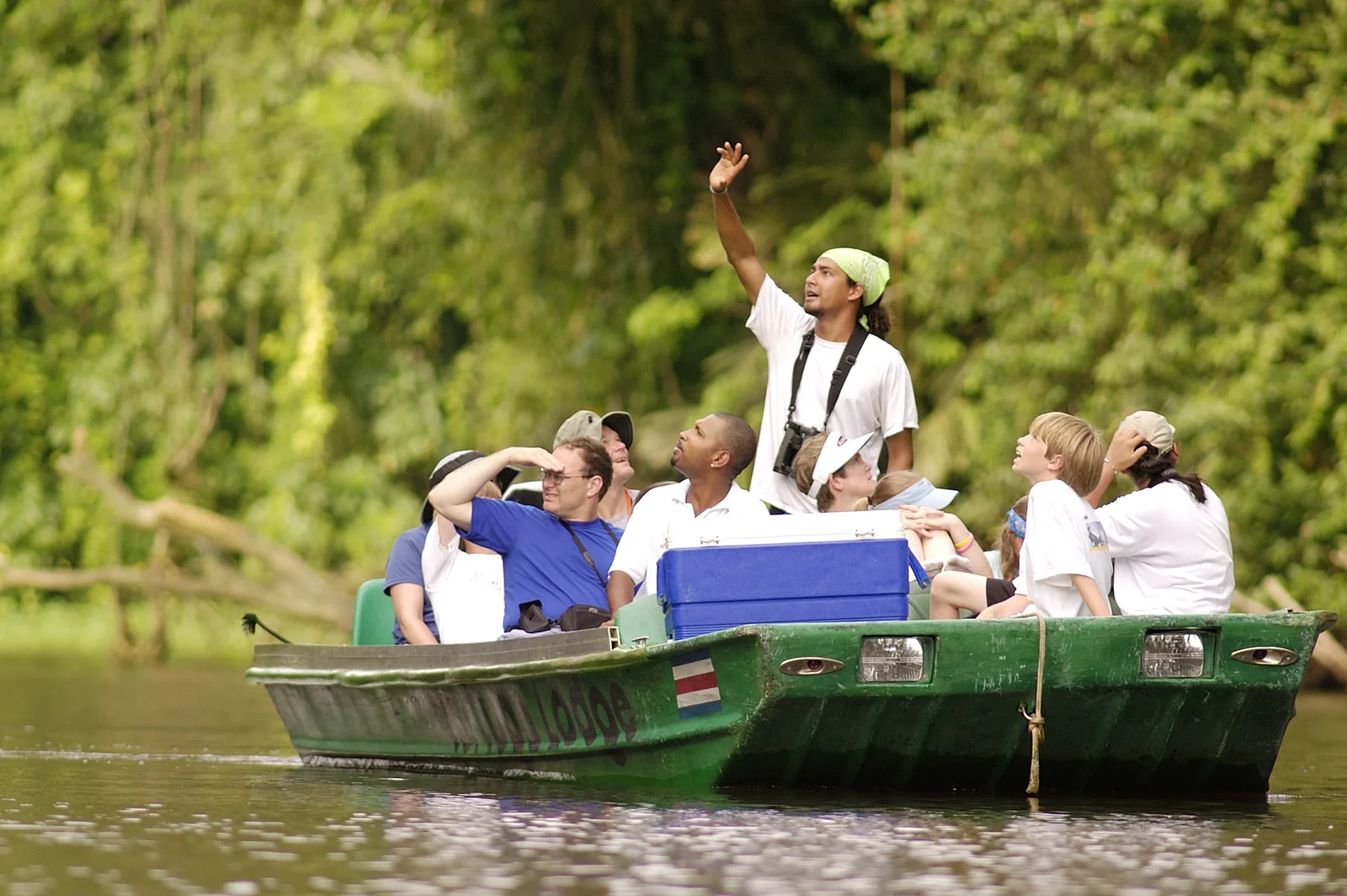 Visitors travel by boat along a narrow channel through tropical vegetation.