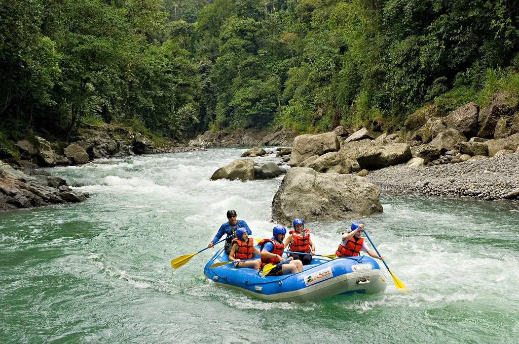 A group paddles a raft through green river rapids.