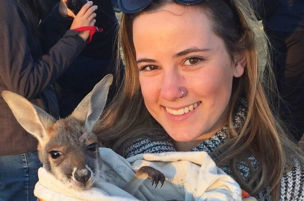 A woman cradles a young kangaroo outdoors.