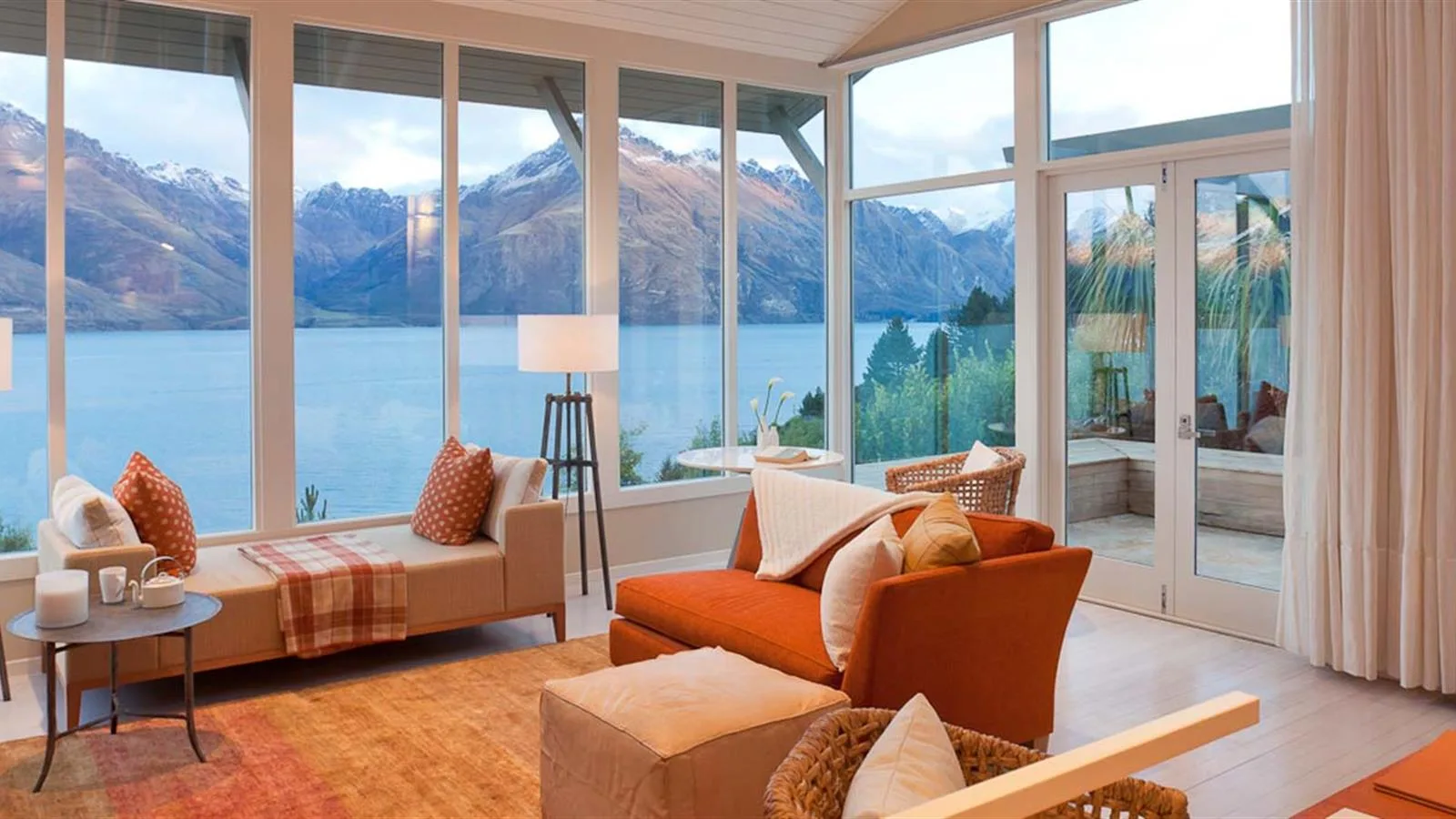 A lounge at Rosewood Matakauri with floor-to-ceiling windows overlooking Lake Wakatipu and surrounding mountains.