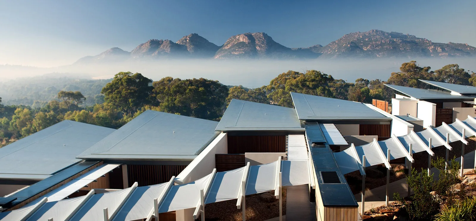 A covered lodge terrace looks out over a Tasmanian bay and wooded hills.