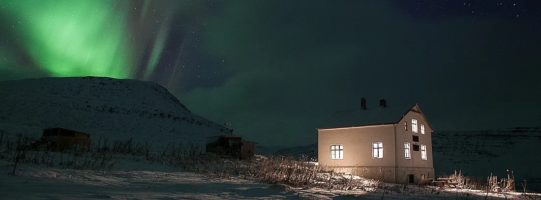 A small remote farmhouse beside an Icelandic fjord beneath the northern lights.
