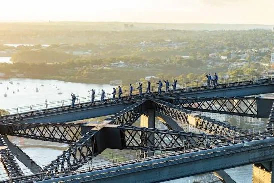 A group of climbers walking along the upper arch of Sydney Harbour Bridge above the harbour.