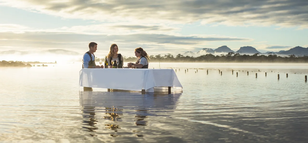 People gathered around a white-clothed table standing in shallow coastal water.