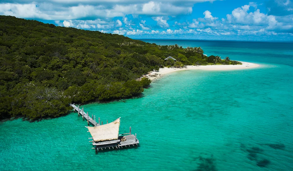 A timber jetty extending from a forested island into turquoise water.