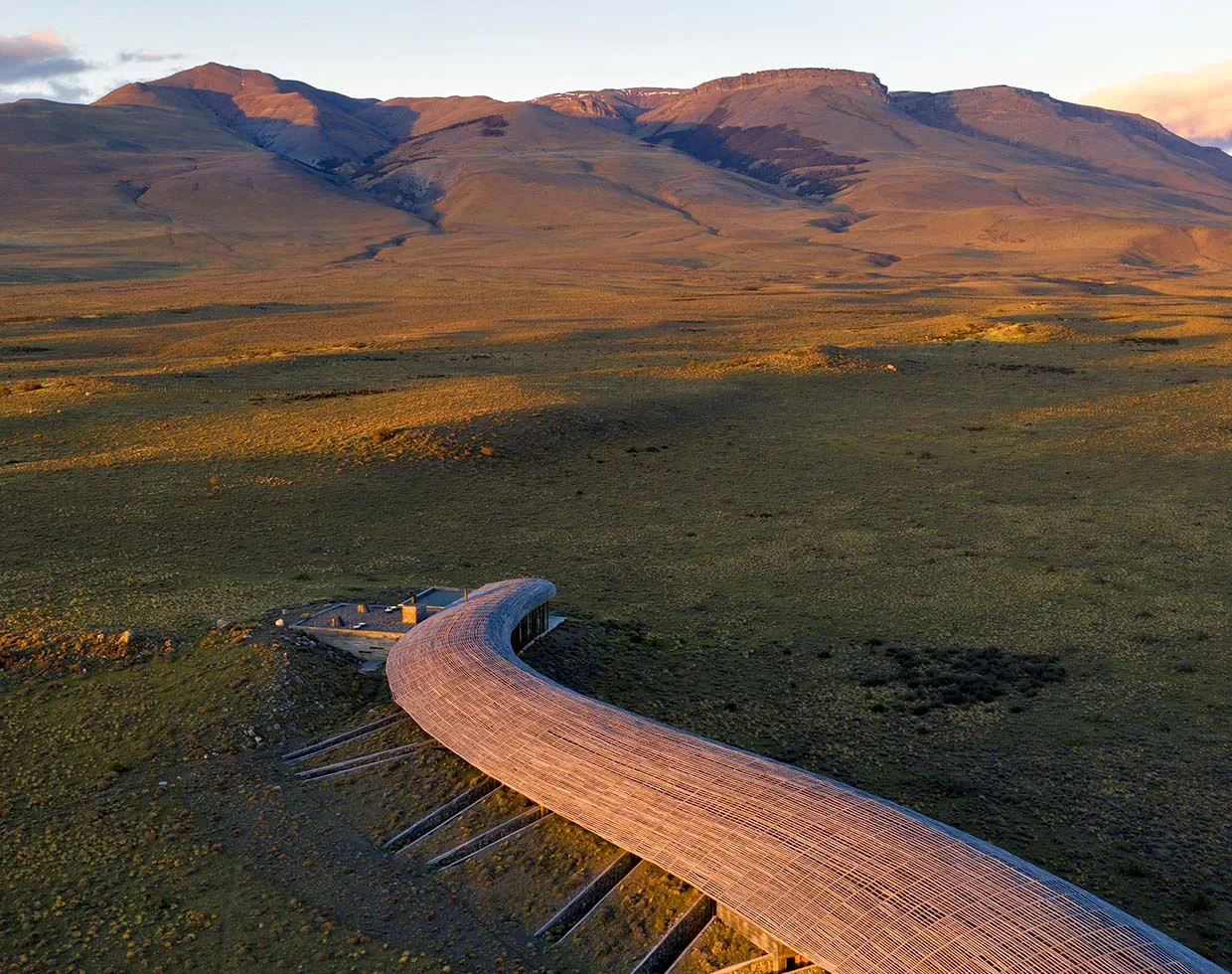 A curved timber lodge set within an open Patagonian landscape.