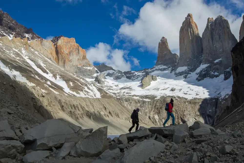 Hikers crossing rocky ground beneath towering granite peaks.