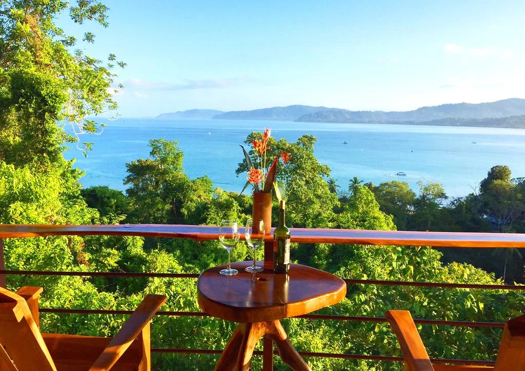 A shaded terrace overlooking trees and a blue coastal bay.