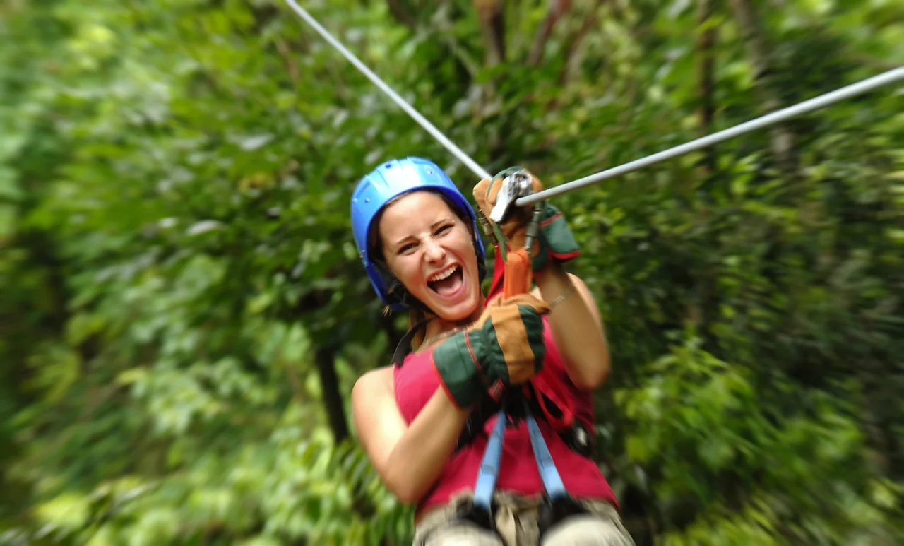A person wearing a helmet and harness on a rainforest zip line.