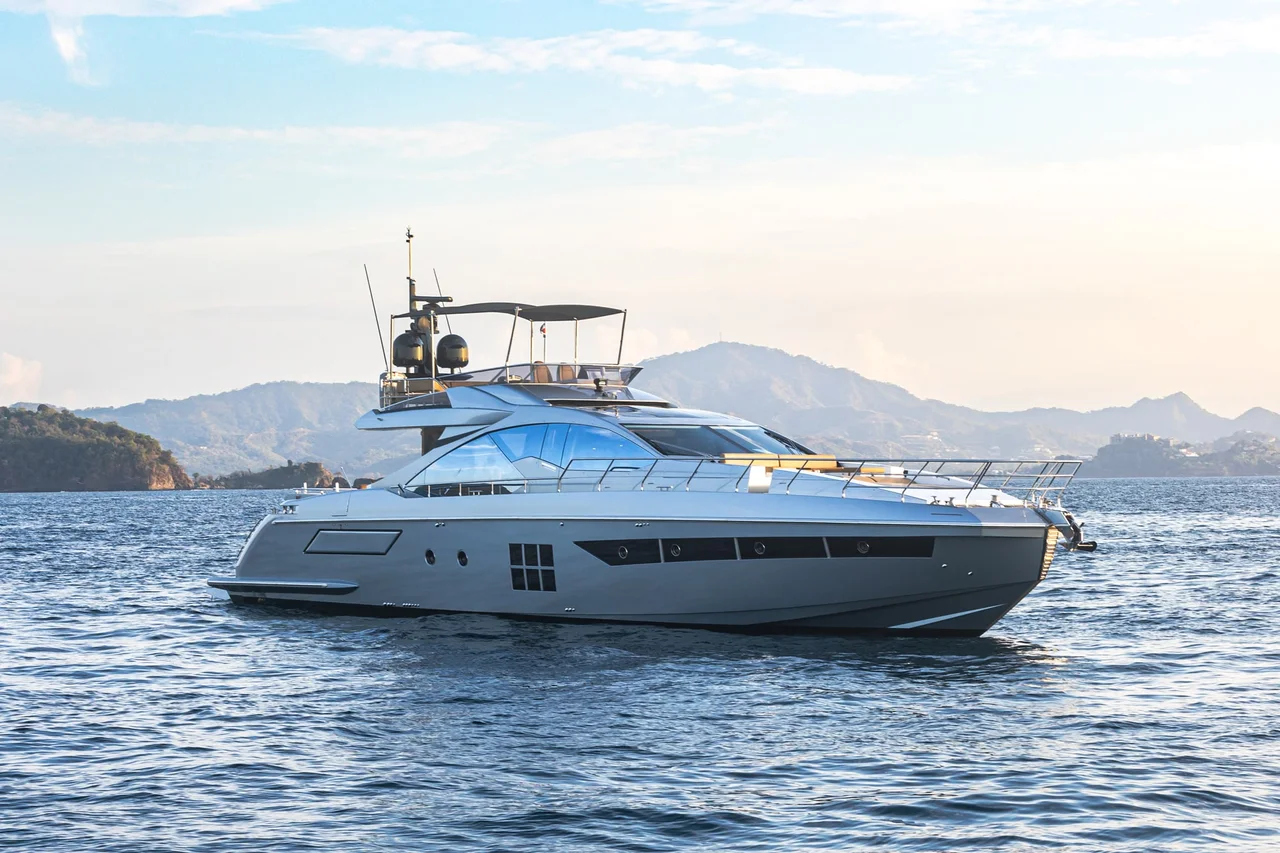 A motor yacht on calm blue water with coastal hills in the background.