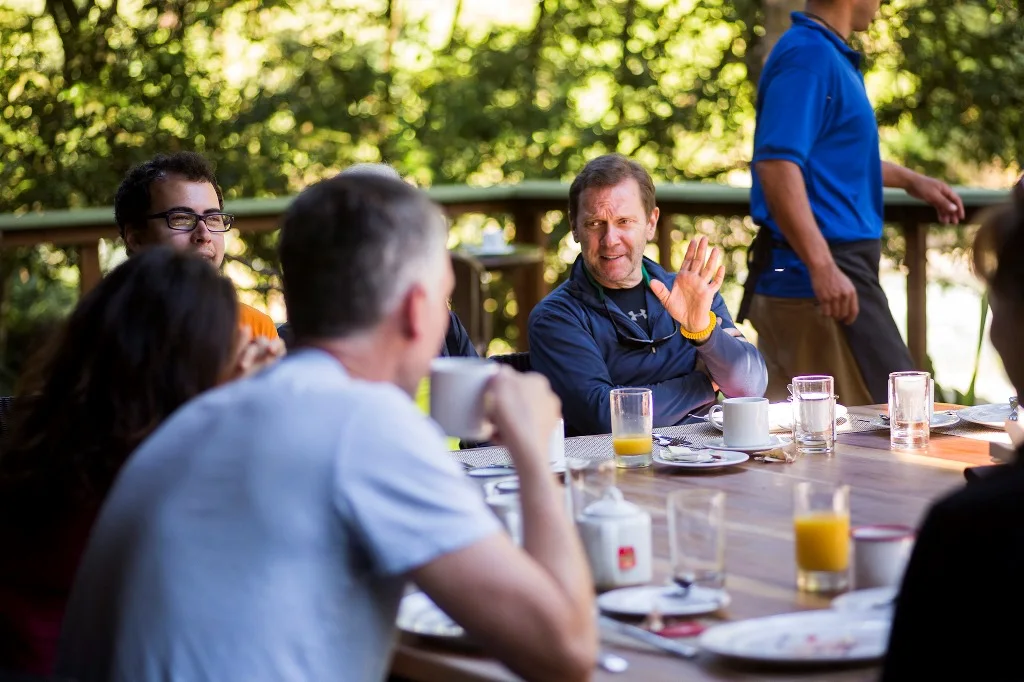 Guests sharing an outdoor meal beneath leafy trees.