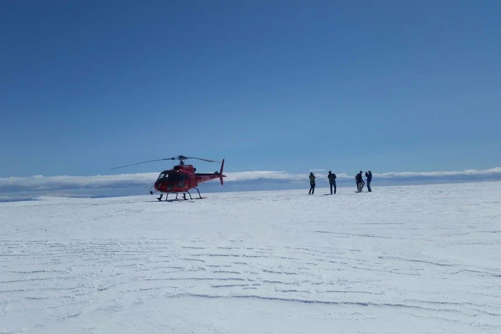 A red helicopter and a small group of people on a broad snowy glacier.