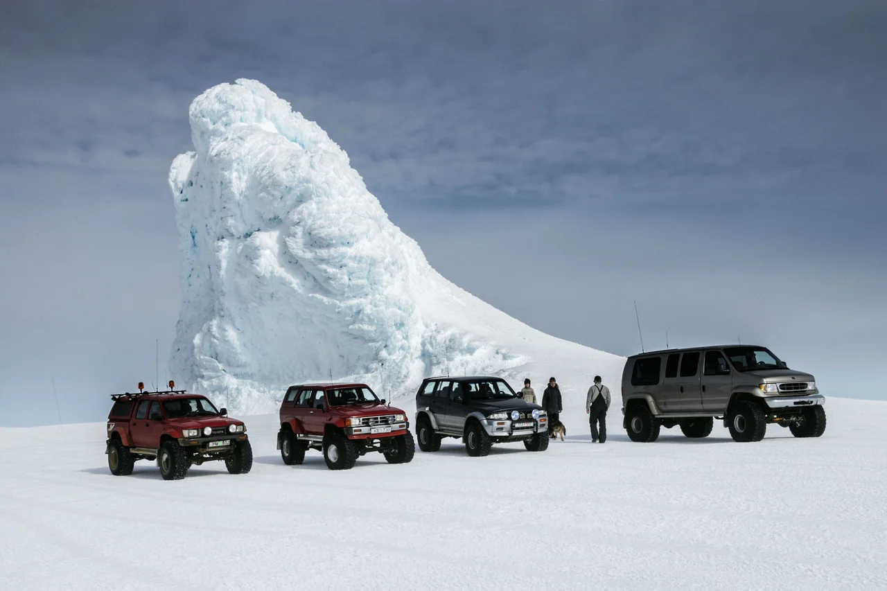 Off-road vehicles and people beside a towering ice formation on snowy terrain.
