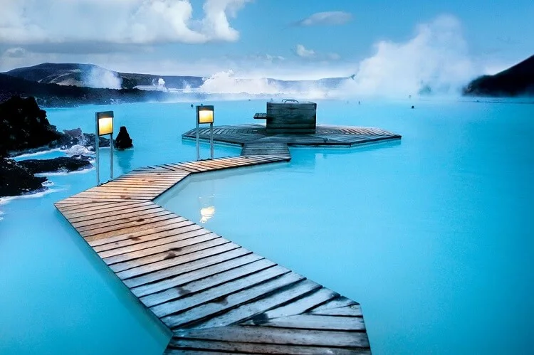 A wooden walkway crossing milky blue geothermal water with steam rising beyond.