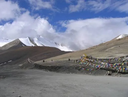 Colourful prayer flags beside a road through a barren mountain pass beneath clouds.