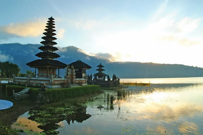 A lakeside temple with a tiered roof reflected in still water beneath mountains.