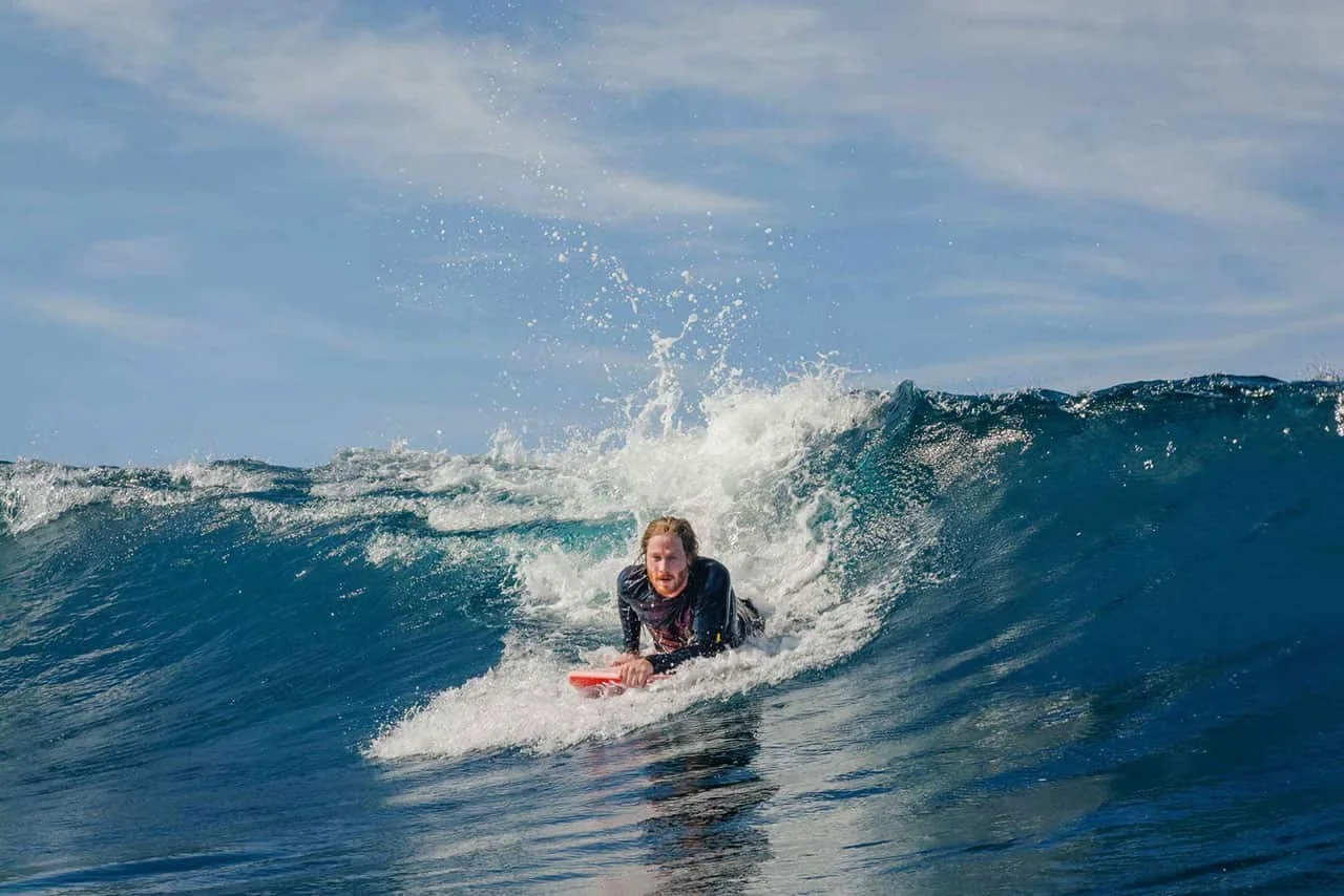 A person riding a wave on a bodyboard beside a breaking crest.
