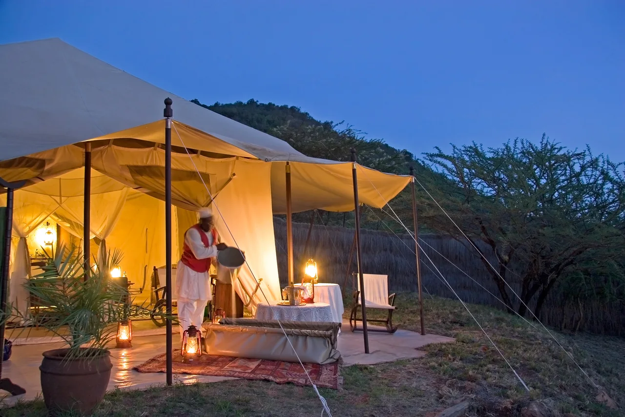 A safari tent illuminated at dusk, with people at its entrance.