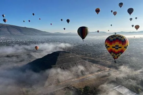 Hot-air balloons floating above pyramids and mist-covered terrain.