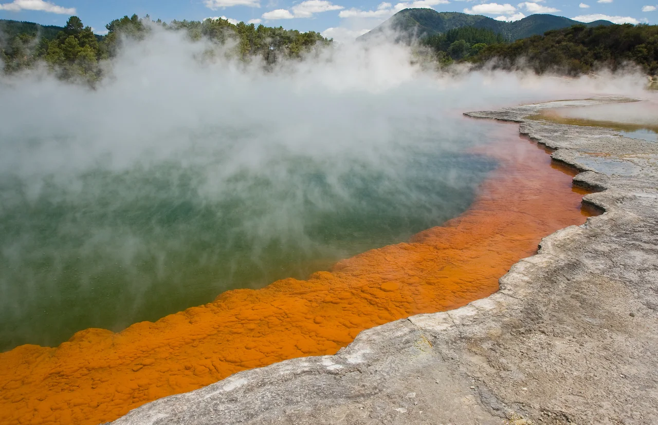 Steam rising above a geothermal pool with a vivid orange mineral edge.