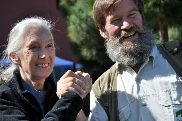 Two people smiling together outdoors, one with a beard and one with white hair.