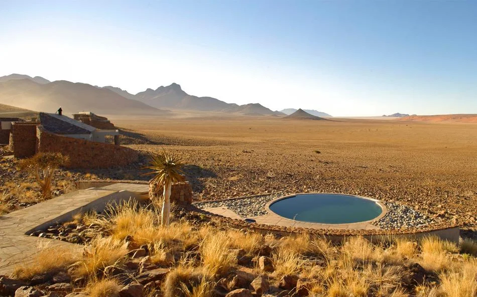 A circular pool overlooking an open desert plain and distant mountains.