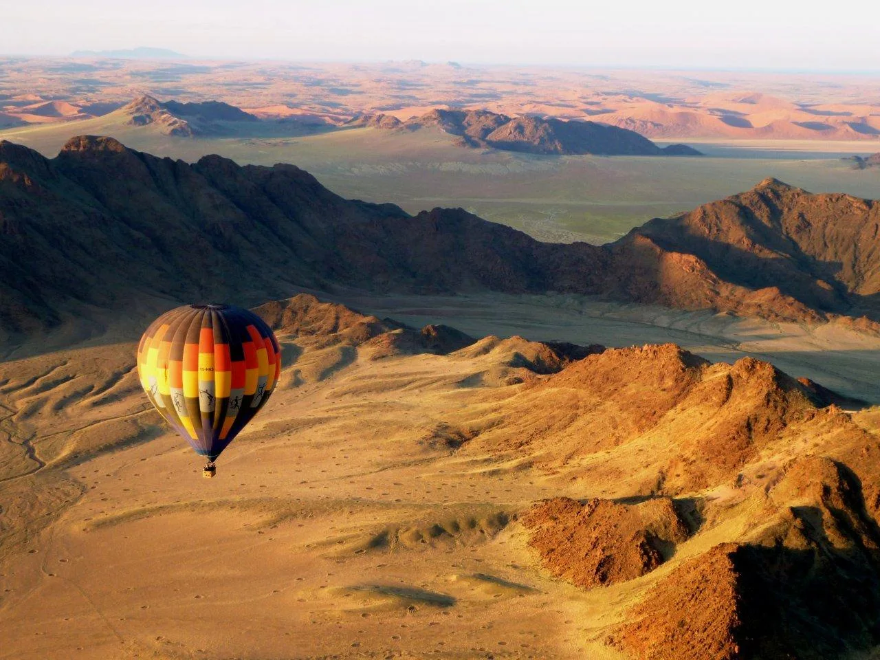 A colourful hot-air balloon floating over a rocky desert landscape.