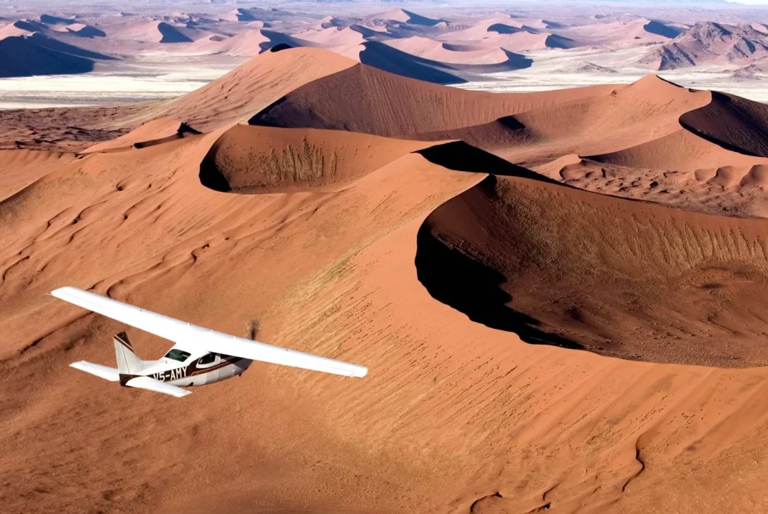 A small propeller aircraft flying above red sand dunes.