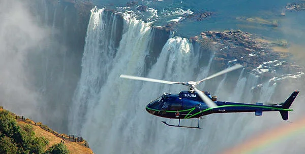 A helicopter flying beside a waterfall and rising spray.