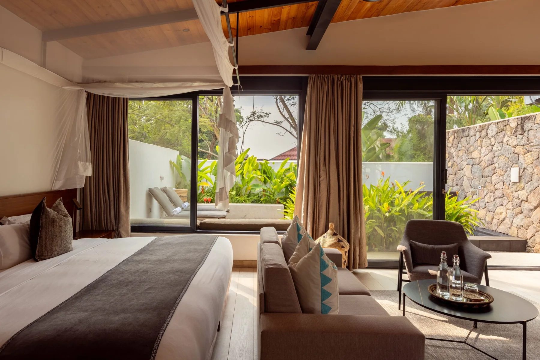 A bedroom with a large bed and seating area opens through glass doors onto a planted terrace.