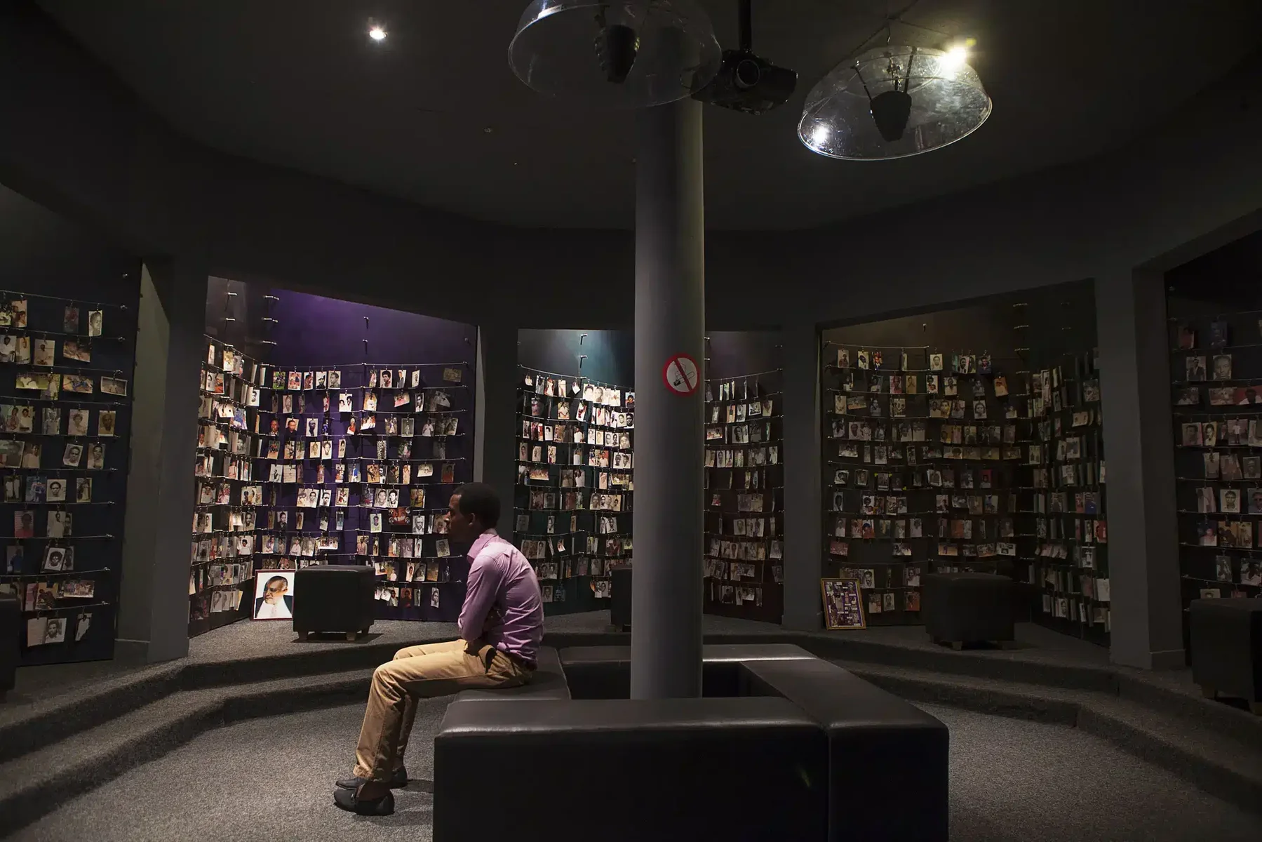A visitor sits in an exhibition room lined with photographs.