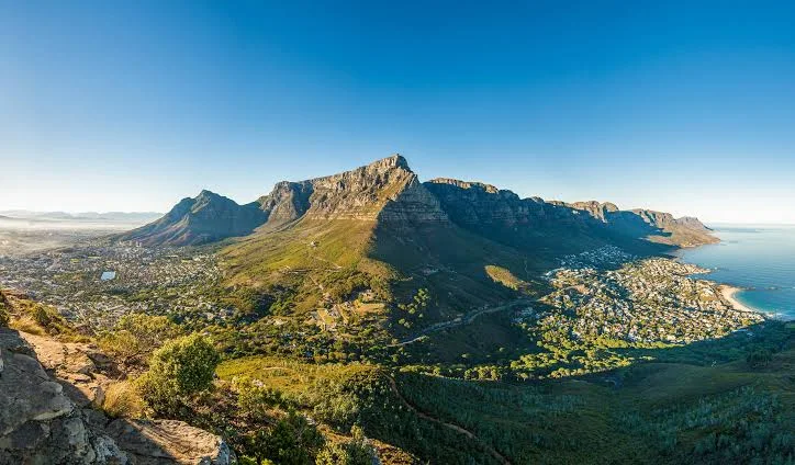 Table Mountain rises above a coastal city and blue bay on a clear day.