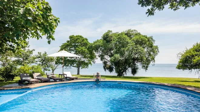 A swimming pool and loungers overlook a tree-lined waterfront.