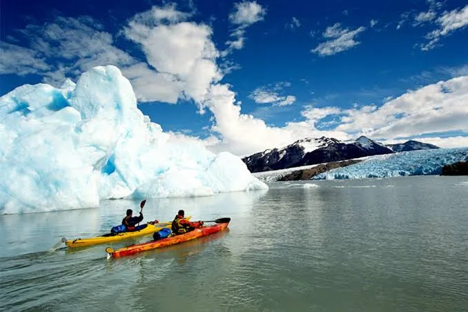 Two kayaks paddle on a glacial lake beside a large iceberg.
