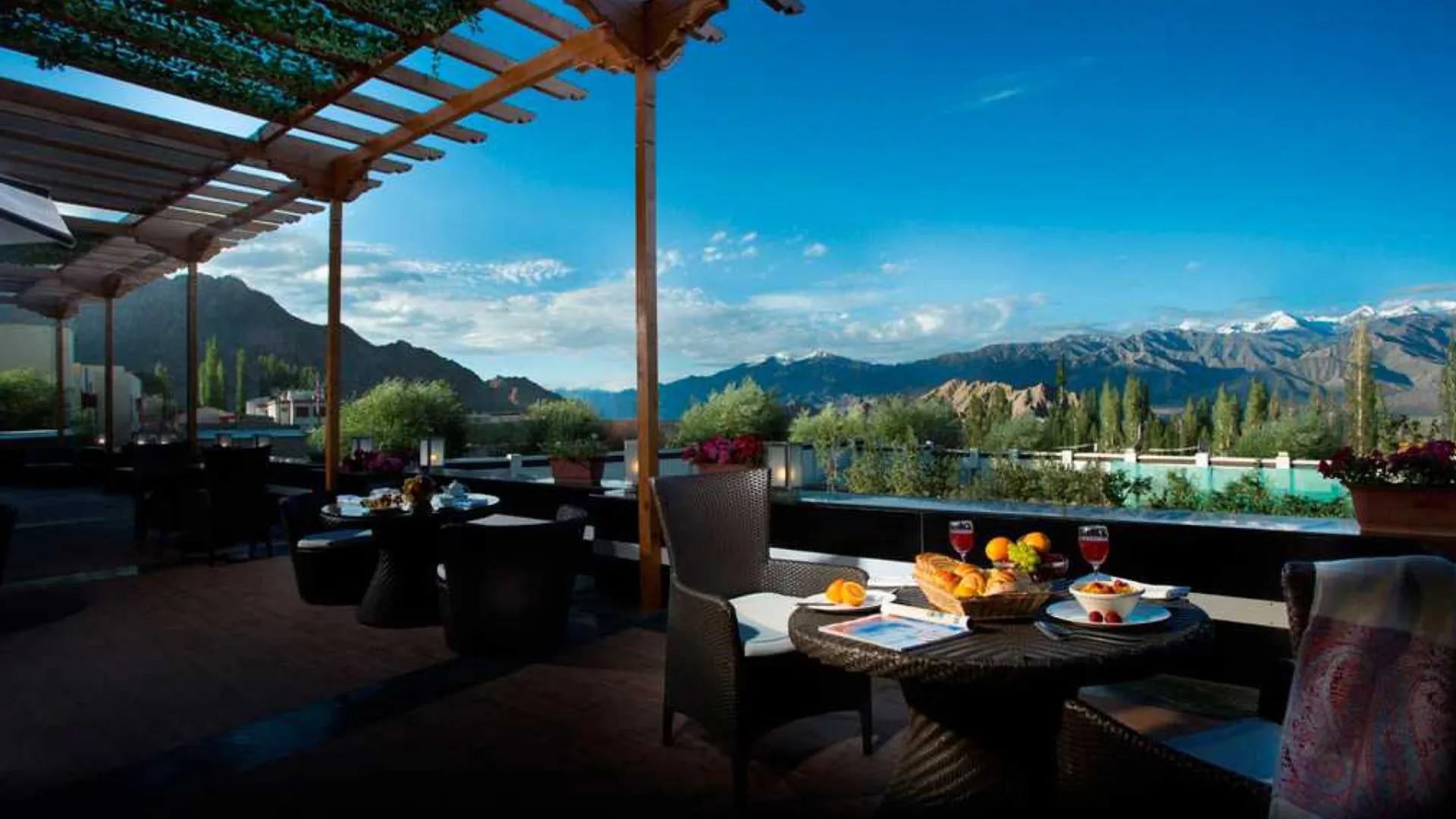 A hotel terrace with dining tables overlooks Leh and snow-covered mountains.