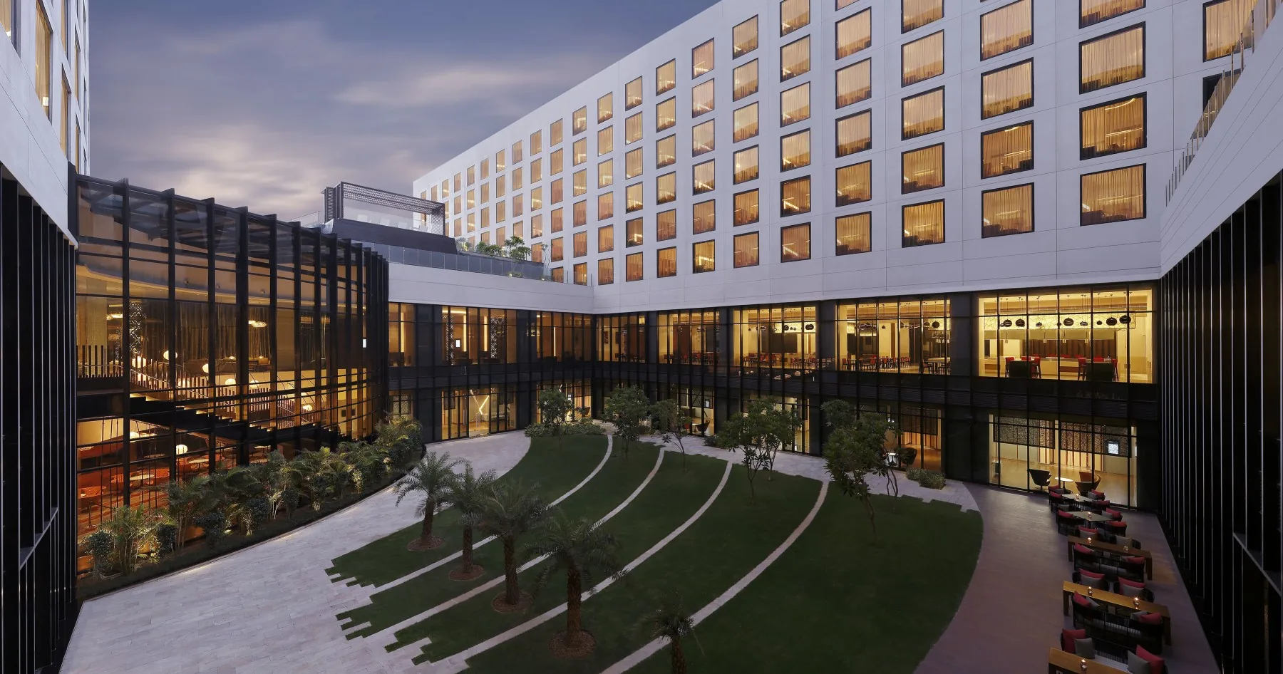 A modern hotel courtyard with planted lawns is surrounded by glass-fronted rooms.