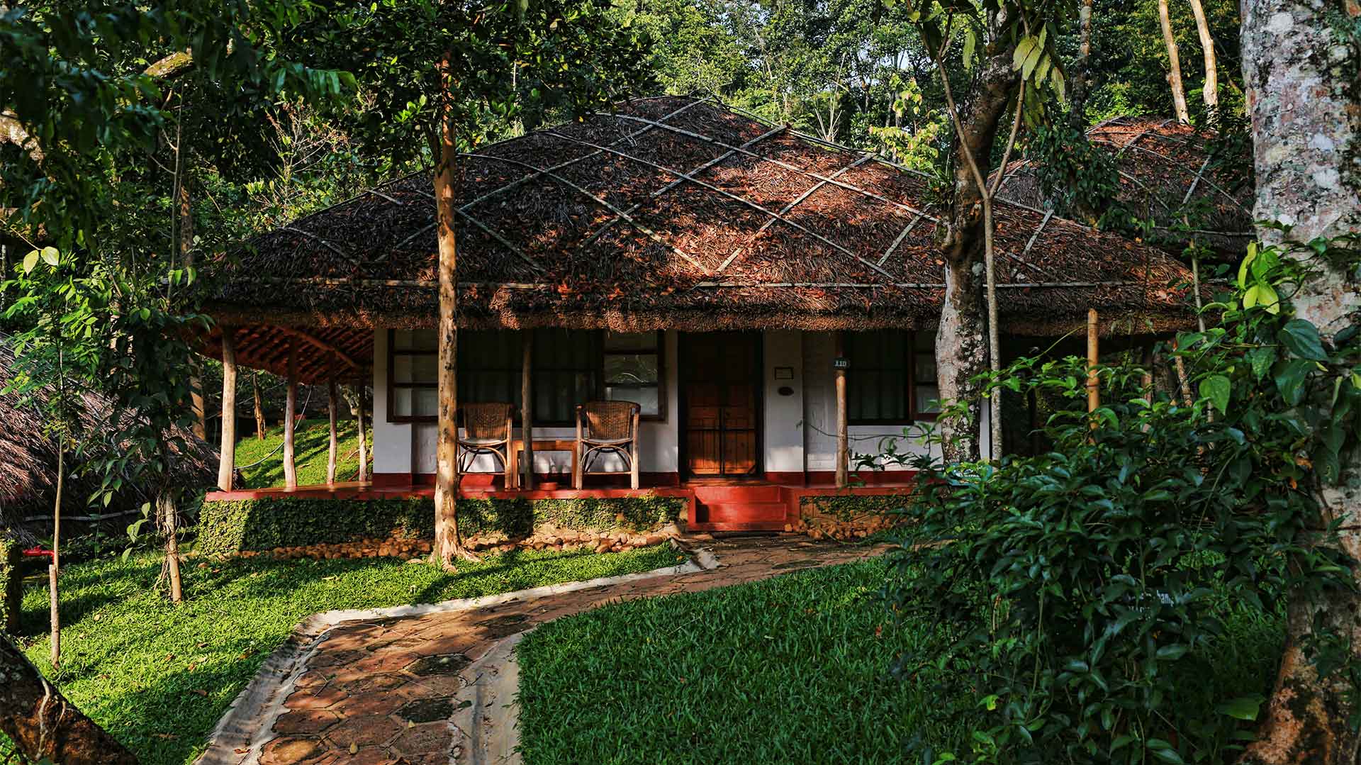 A thatched cottage with a shaded veranda sits among tropical forest.