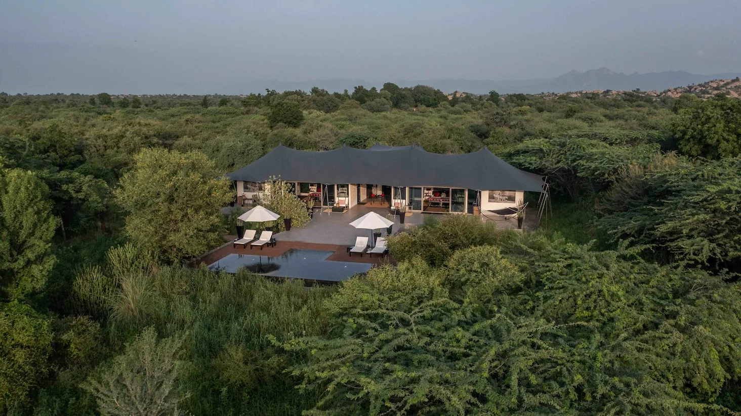 A low-slung lodge pavilion and pool sit amid trees and scrub.